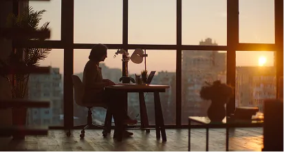 Woman working at a desk in front of a sunset