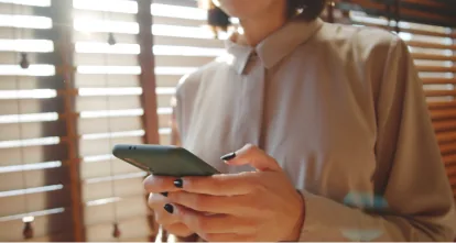 Woman checking her phone beside office blinds